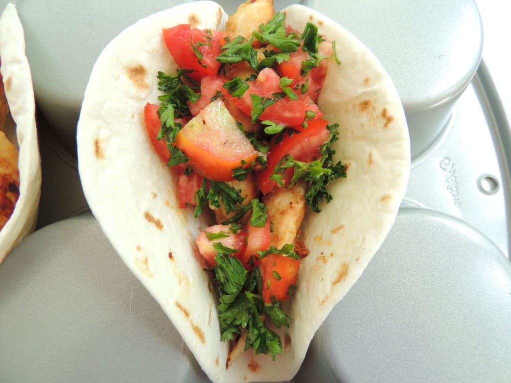 Top Greek chicken tacos with tomato mixture.