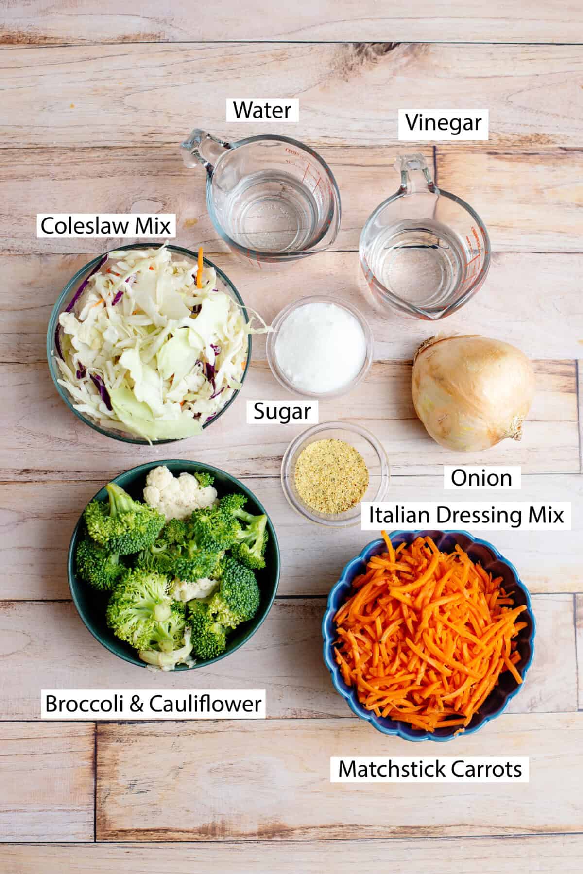 Ingredients for crunchy refrigerator salad, featuring coleslaw, broccoli and cauliflower, carrots, onion, sugar, white vinegar, and Italian seasoning mix.