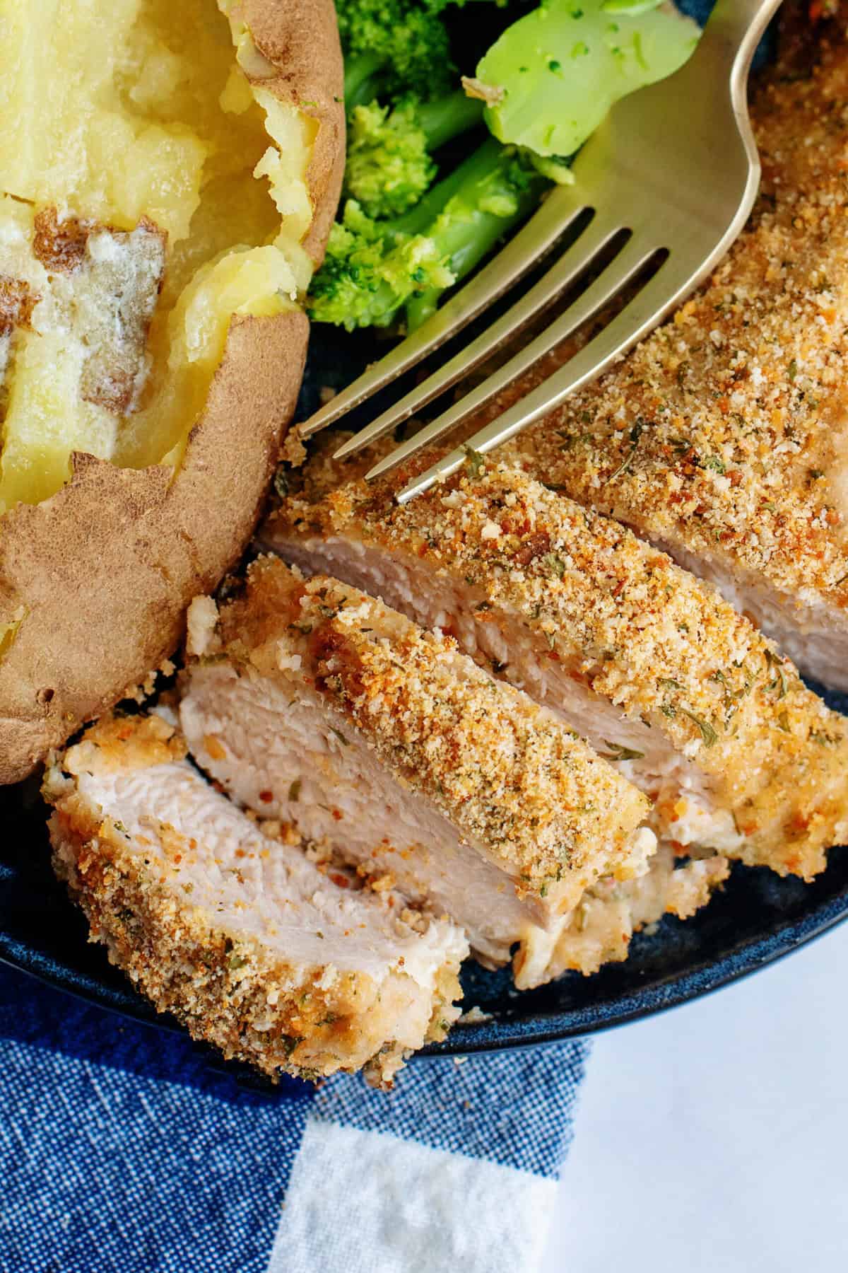 Sliced oven-fried chicken on a blue plate with a baked potato and broccoli on the side.