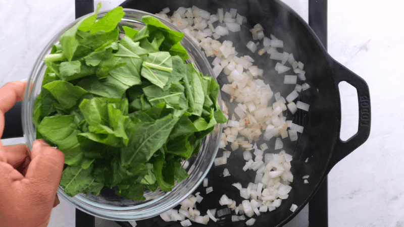 Adding greens to onion in skillet.