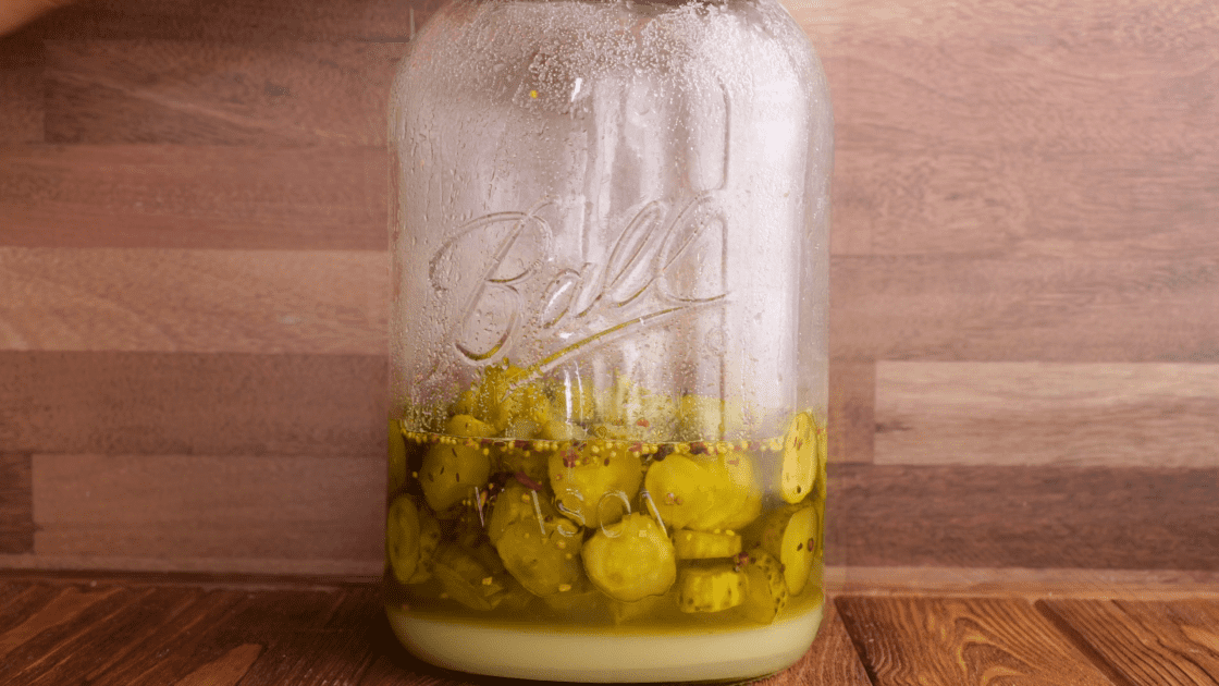 Sweet pickles in jar with sugar at the bottom.