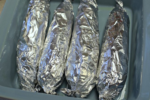 Corns on the cob wrapped in foil and placed in baking dish to bake in the oven.