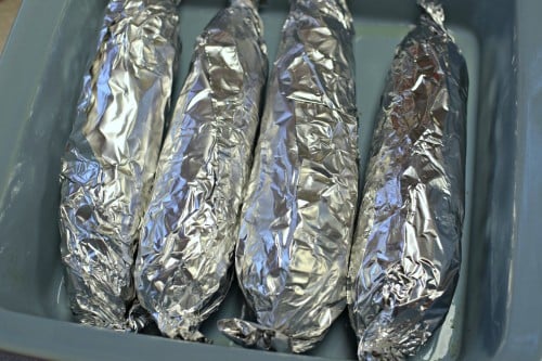 Corns on the cob wrapped in foil and placed in baking dish to bake in the oven.