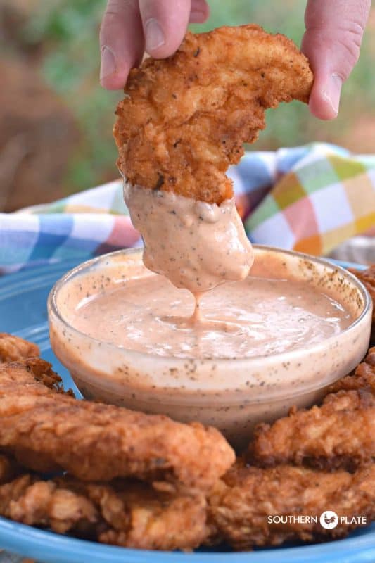 Dipping fried chicken tender in Comeback Sauce.