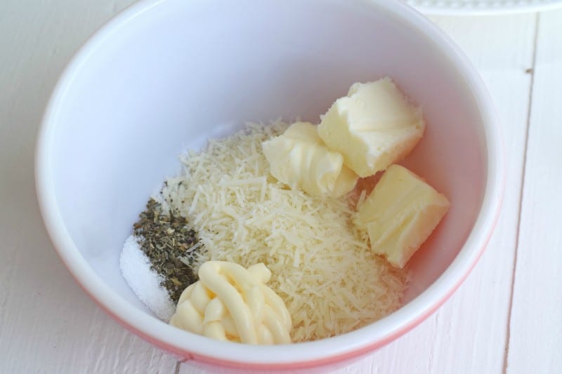 Combine shredded parmesan cheese, mayonnaise, 1/2 of the butter, dried basil, and salt in a mixing bowl.