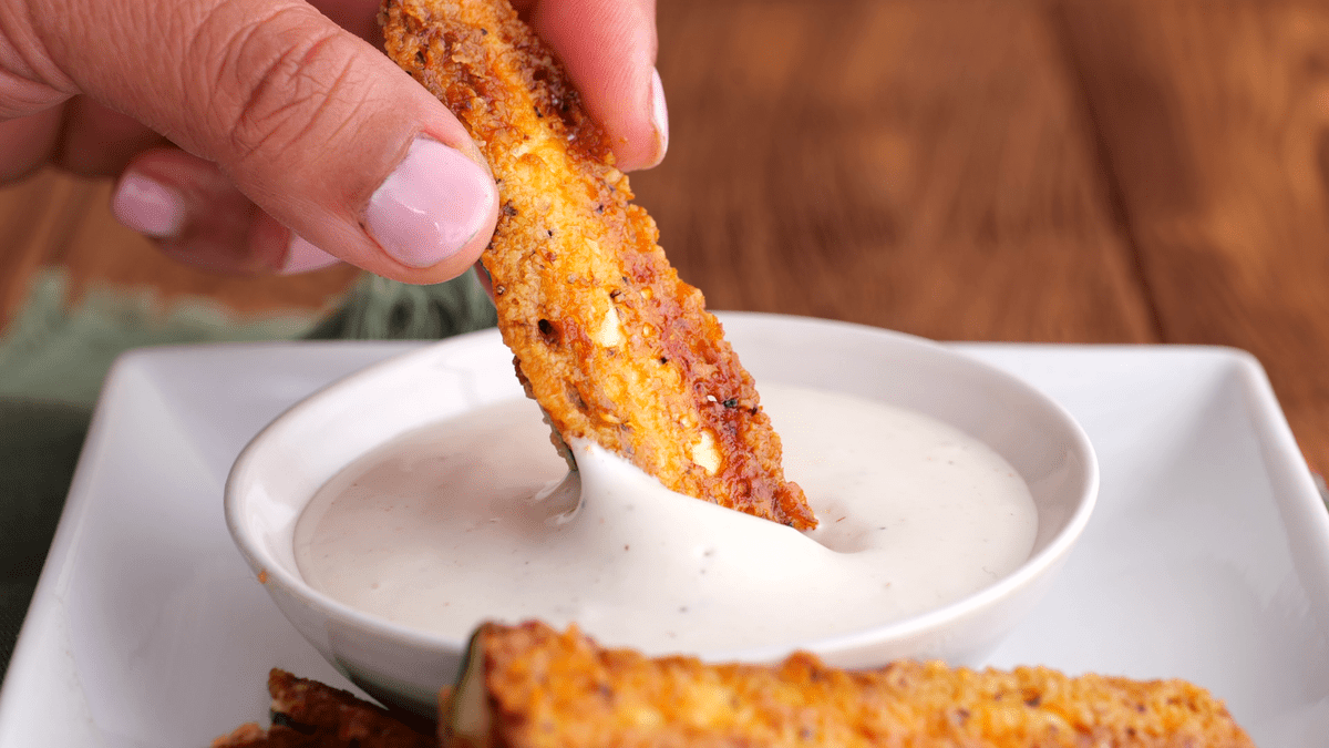 Dipping baked zucchini fries in dressing.