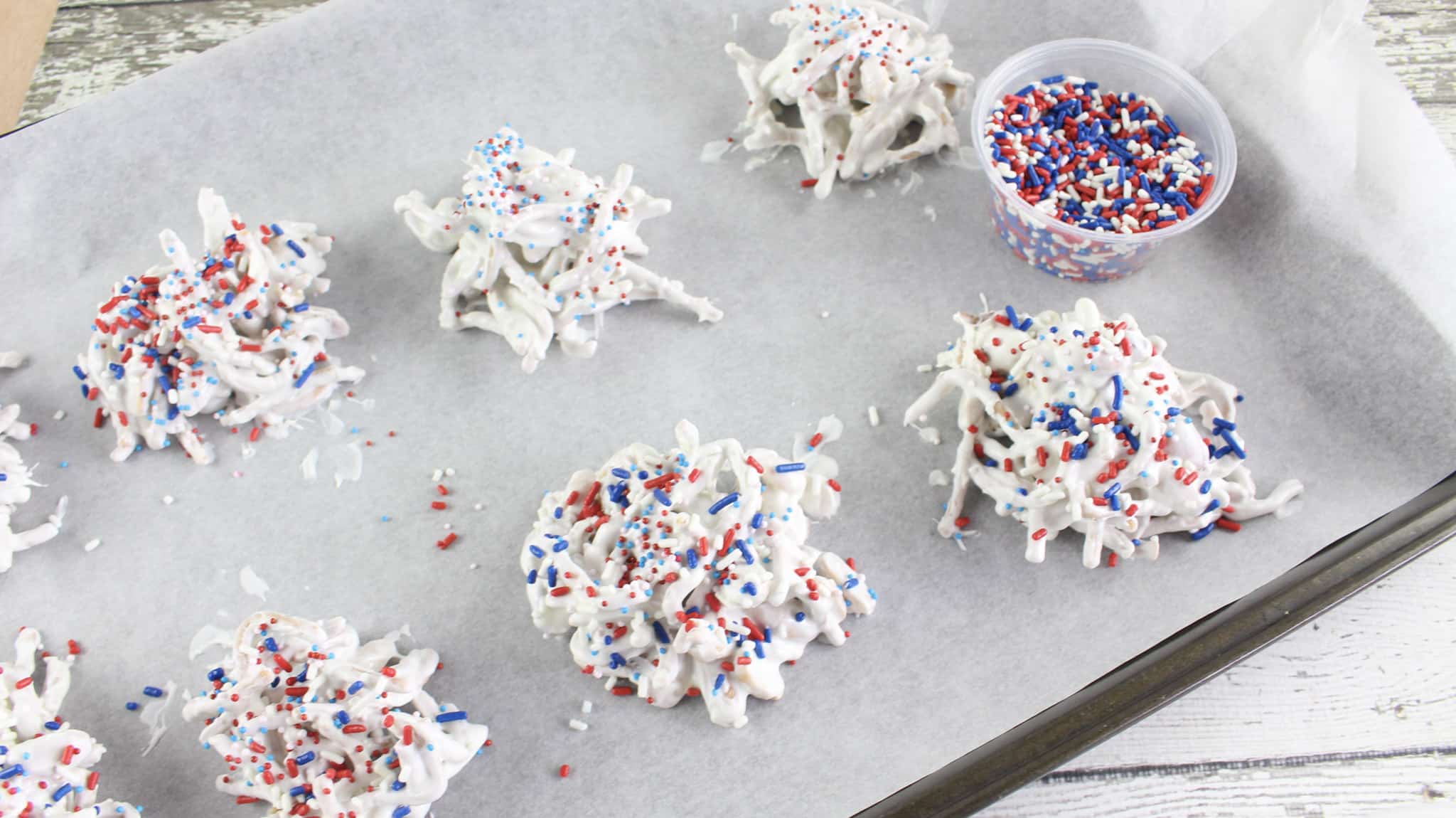 Old glory haystacks candy on a parchment lined baking sheet with patriotic sprinkles.