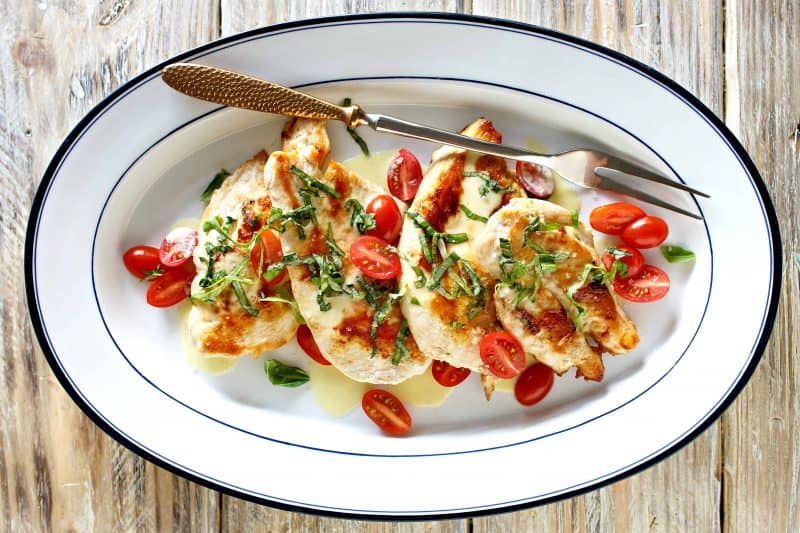 Plate of chicken with fresh basil and tomatoes on top.