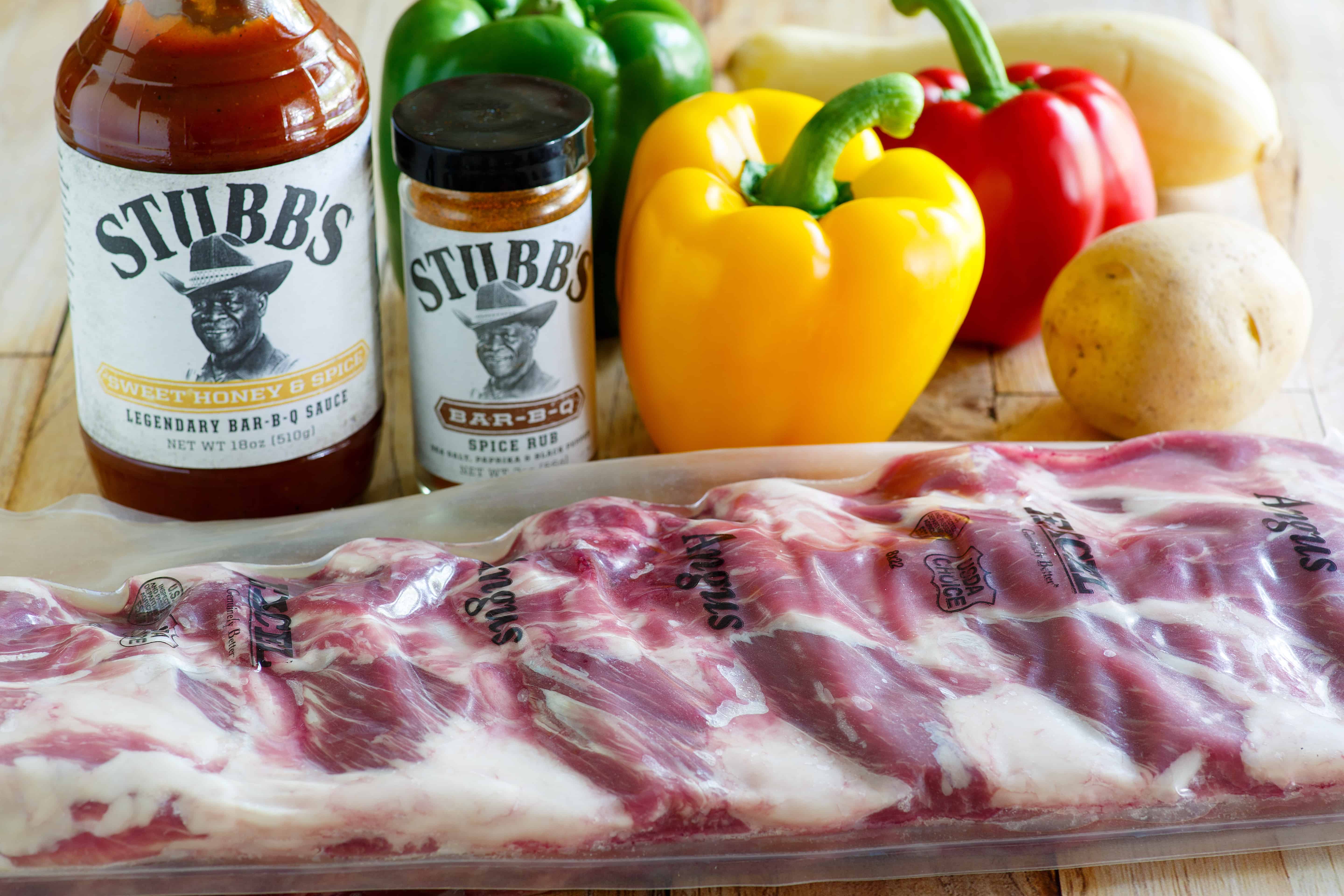 Ingredients for BBQ ribs in the oven with veggies featuring Stubb's BBq sauce, red, green, and yellow bell peppers, squash, and potatoes.