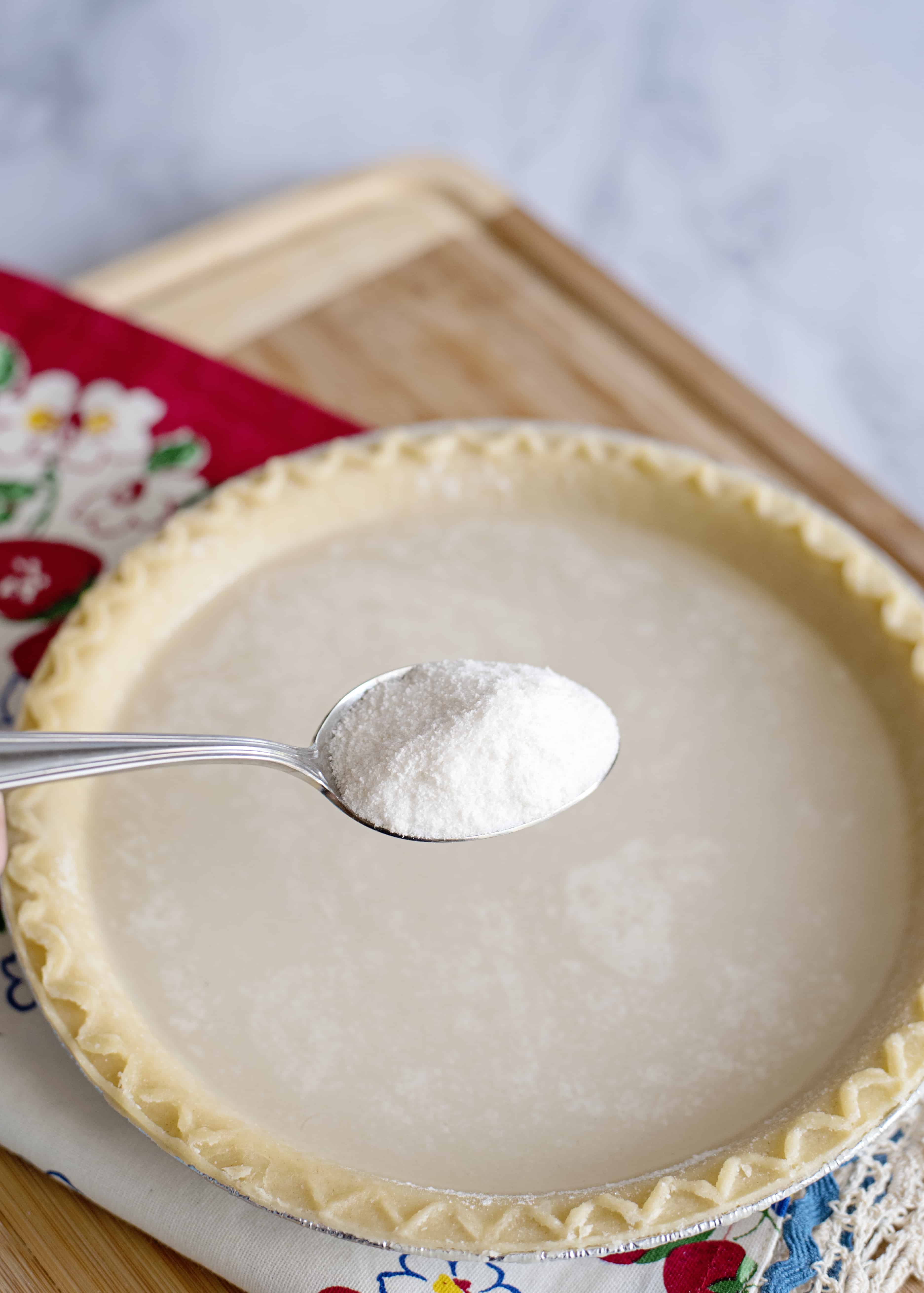 Sprinkling sugar in a pie shell full of water with a spoon.