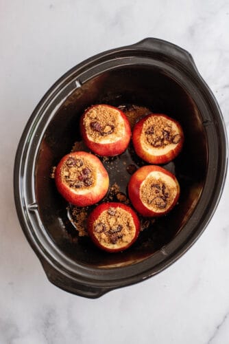 Apples in slow cooker with spoonful or sugar mixture inside each core.