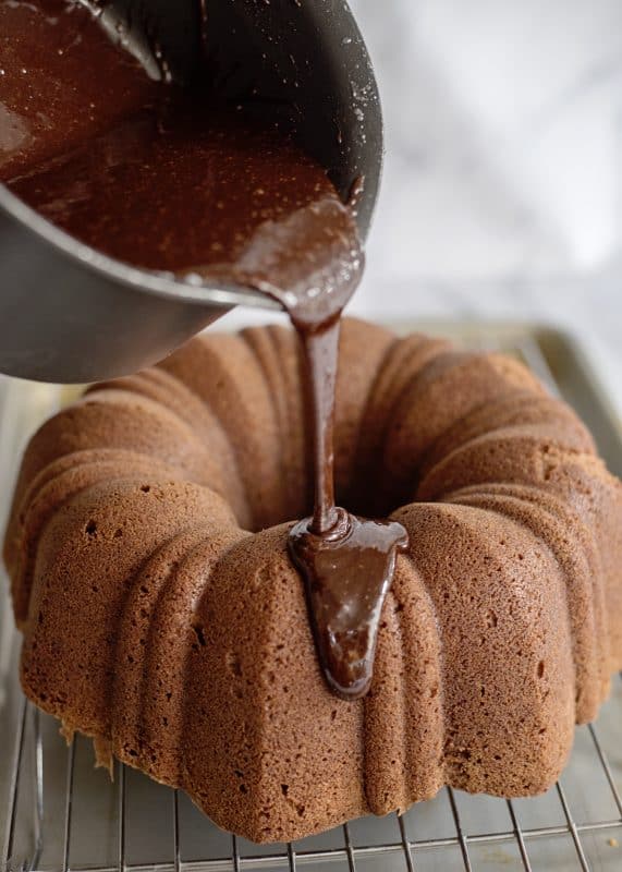 Pouring fudge glaze over chocolate pound cake.