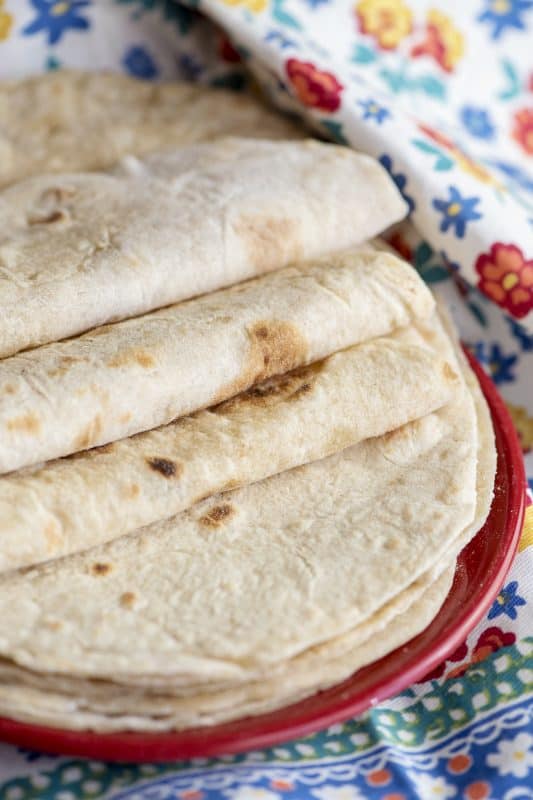 a stack of tortillas on a red plate on a flowery tablecloth 