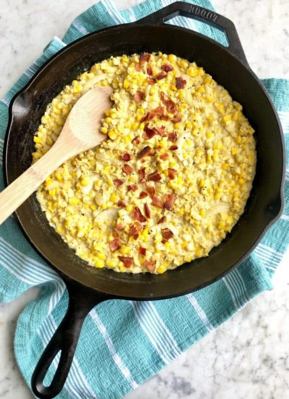 creamed corn in a cast iron skillet with a wooden spoon 