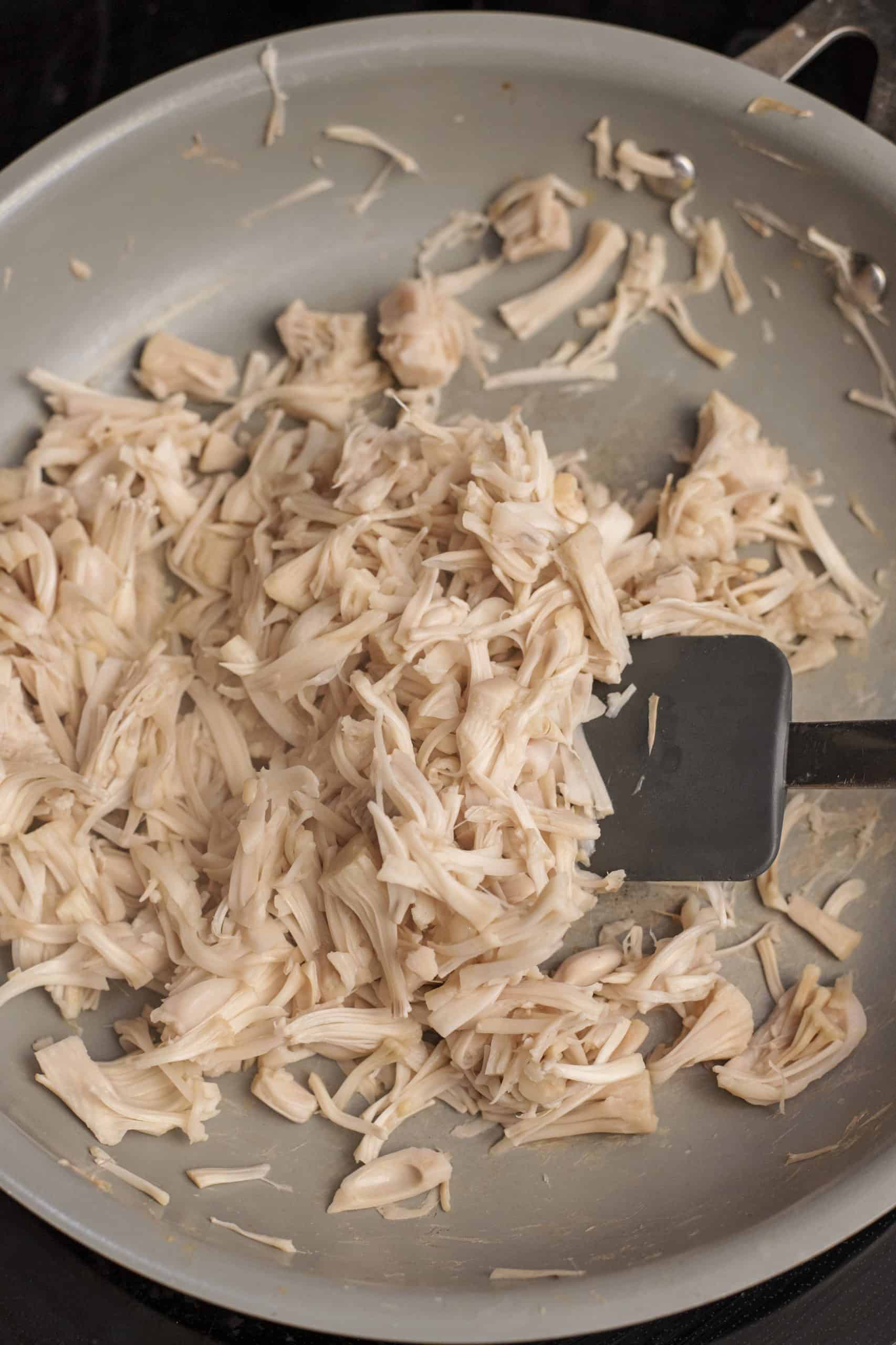 Stirring jackfruit in a skillet with a spatula.