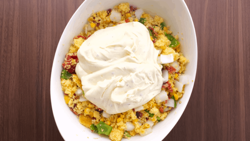 Adding salad dressing to cornbread salad.