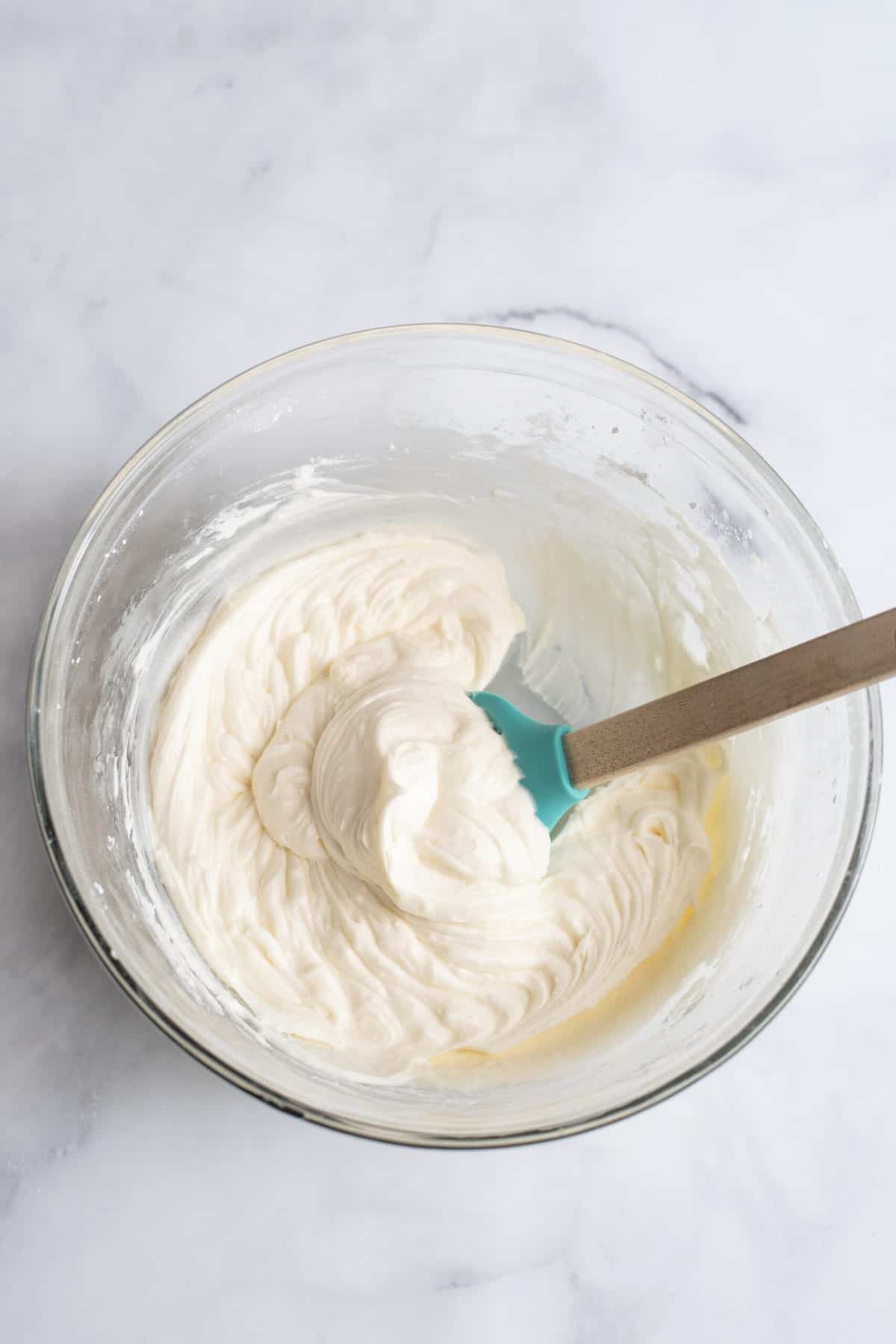 Buttercream frosting in a glass mixing bowl with a spatula.