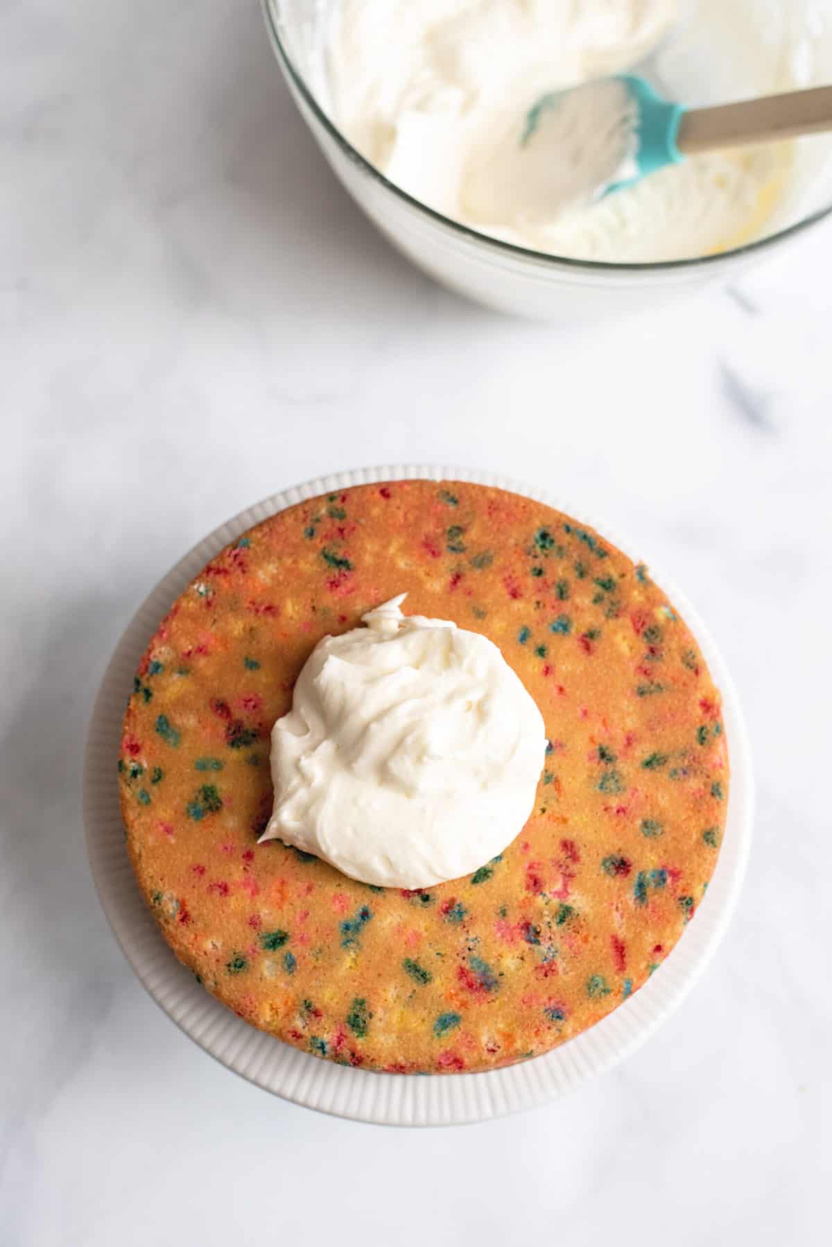 Easy Peasy Birthday Cake From Scratch A big glob of icing on top of a baked rainbow sprinkle-filled cake.