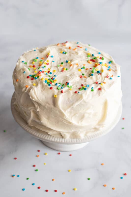 Add sprinkles to frosting on birthday cake.