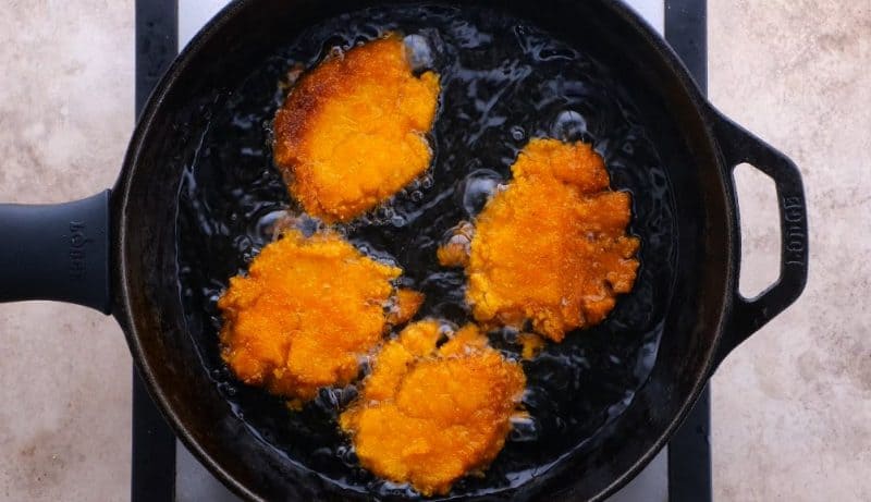 hot water cornbread pieces cooking in oil in skillet.