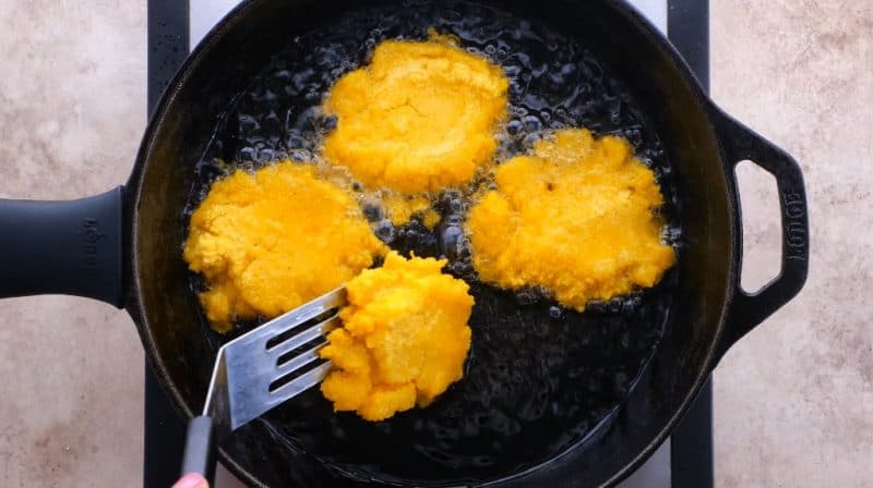 hot water cornbread pieces cooking in oil in skillet.