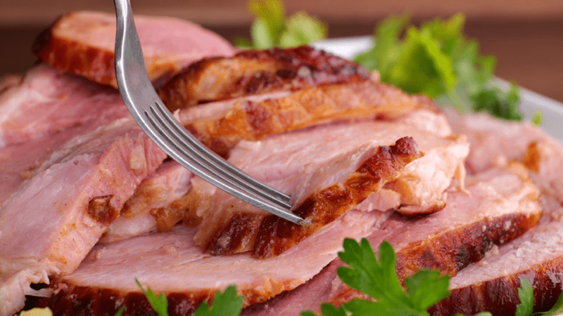 Fork picking up piece of baked ham (hero image for recipes with ham leftovers).