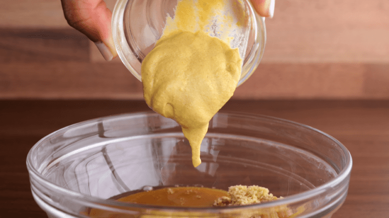 Adding mustard to glaze ingredients in mixing bowl.
