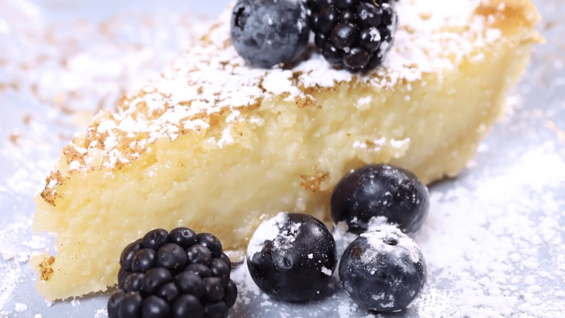 Close-up of slice of buttermilk chess pie with berries and icing sugar.
