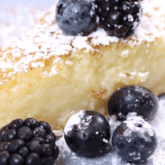 Close-up of slice of buttermilk pie with berries and icing sugar.
