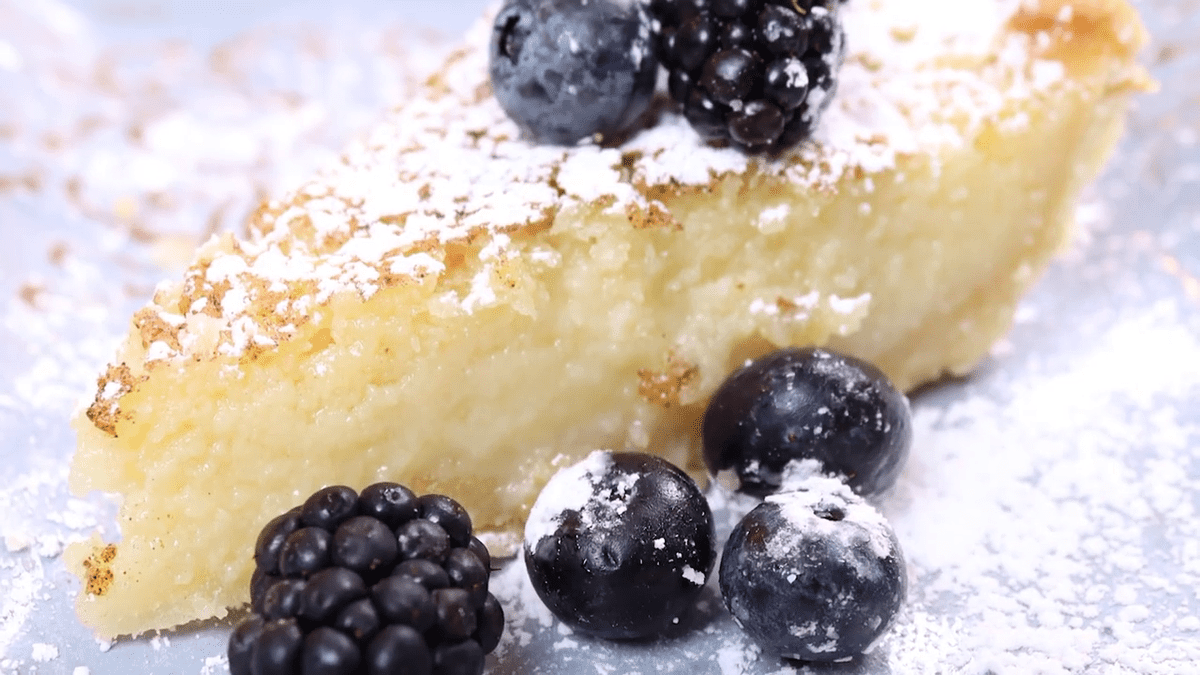 Close-up of slice of buttermilk pie with berries and icing sugar.