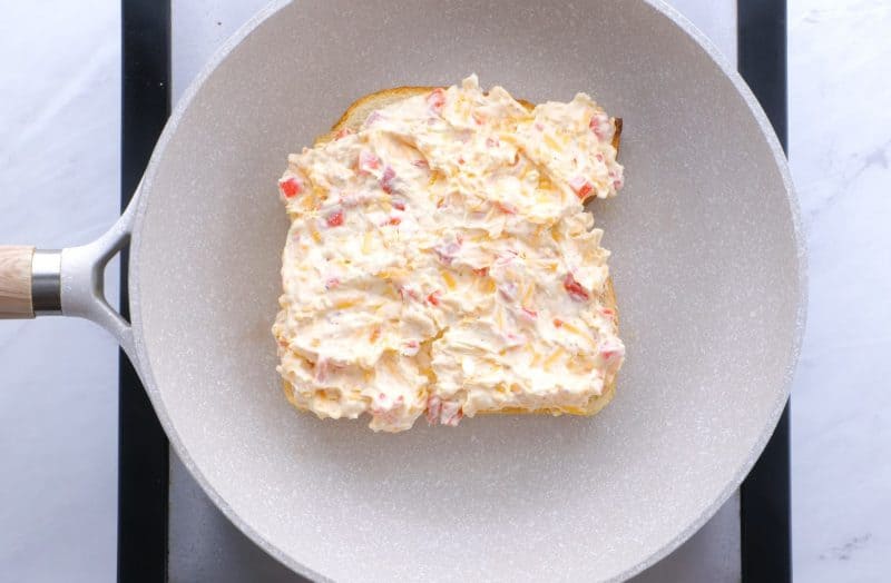 Pimento cheese spread on slice of bread in skillet.