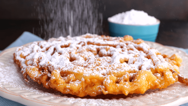 Sprinkle funnel cakes with sugar.