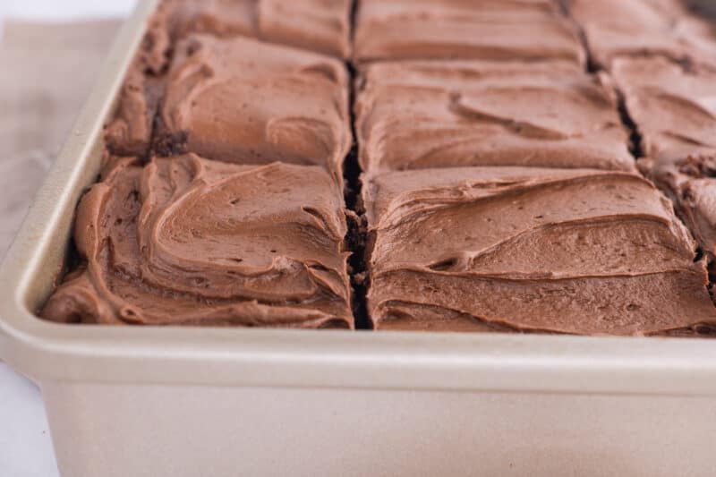 Creamy chocolate frosting on brownie slices in pan.
