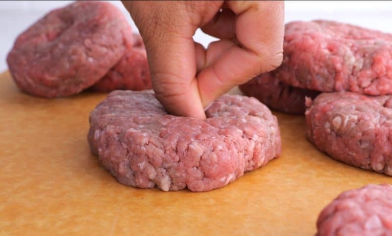 hand putting a hole in the middle of a raw hamburger patty