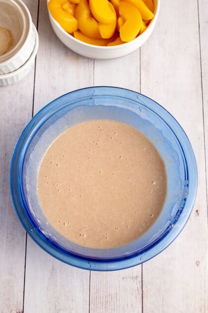 Old-fashioned peach cobbler batter in a glass blue mixing bowl.