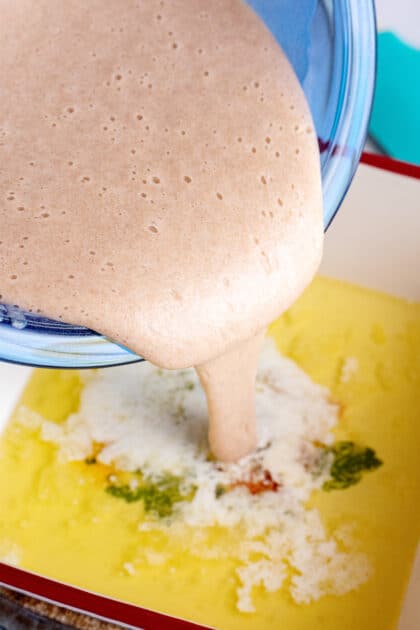 Pouring old-fashioned peach cobbler batter into a baking dish of melted butter.