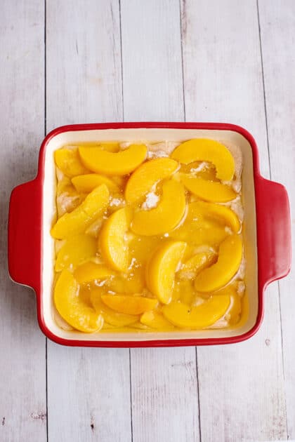 Peaches arranged on a baking dish of batter and melted butter.