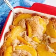 Serving spoon sticking out of baked old-fashioned peach cobbler.