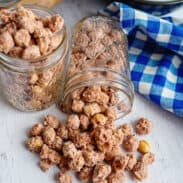 Candied peanuts spilling out of a glass mason jar onto a wooden serving board.