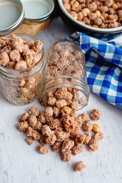 Candied peanuts spilling out of a glass mason jar onto a wooden serving board.