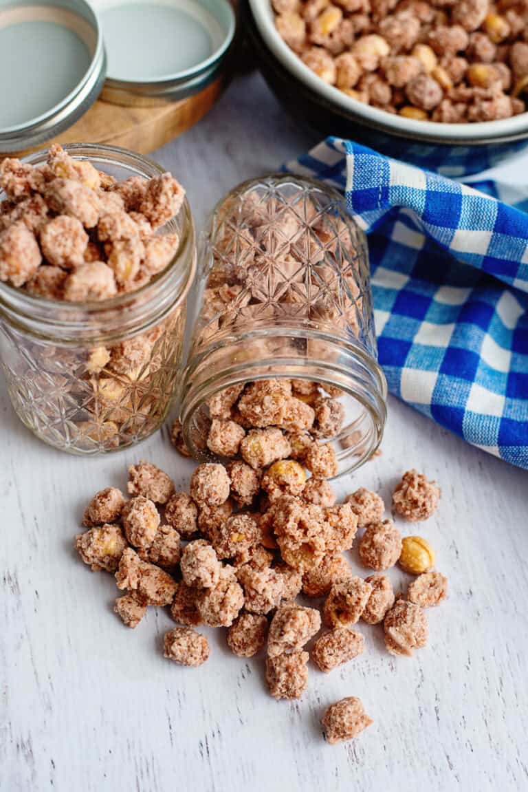 Candied peanuts spilling out of a glass mason jar onto a wooden serving board.