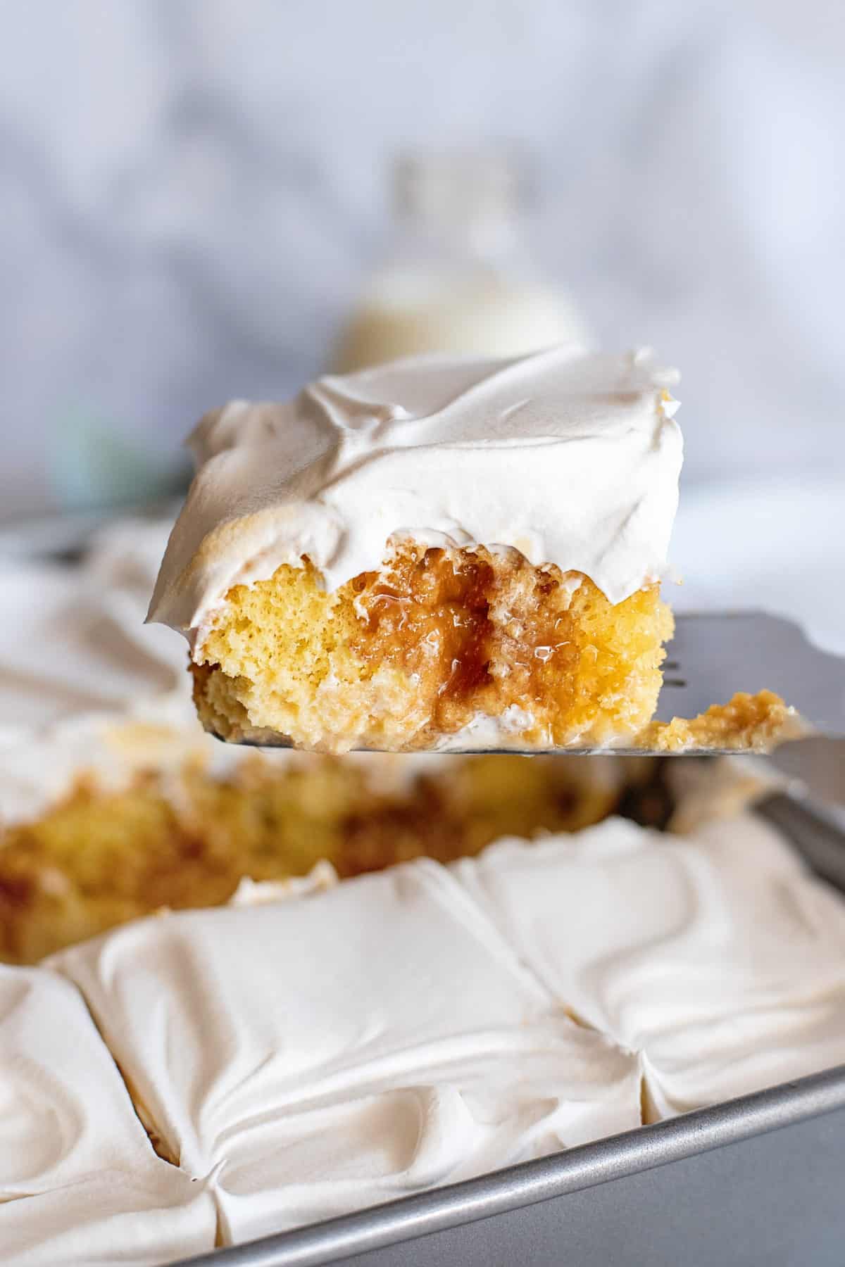 A spatula lifting a slice of cuatro leches cake out of a sheet pan.