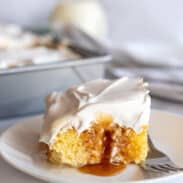 A slice of cuatro leches cake on a plate with caramel sauce oozing out.