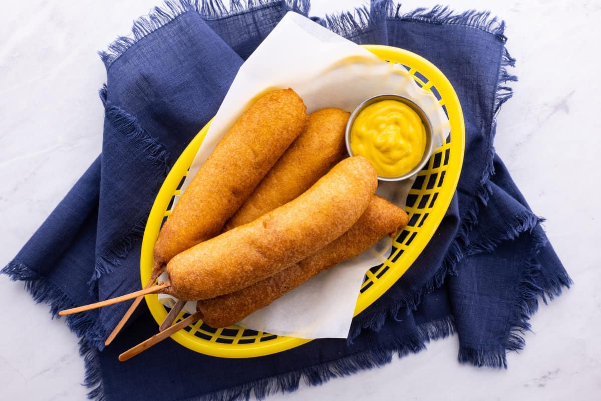 Basket of corn dogs with mustard.