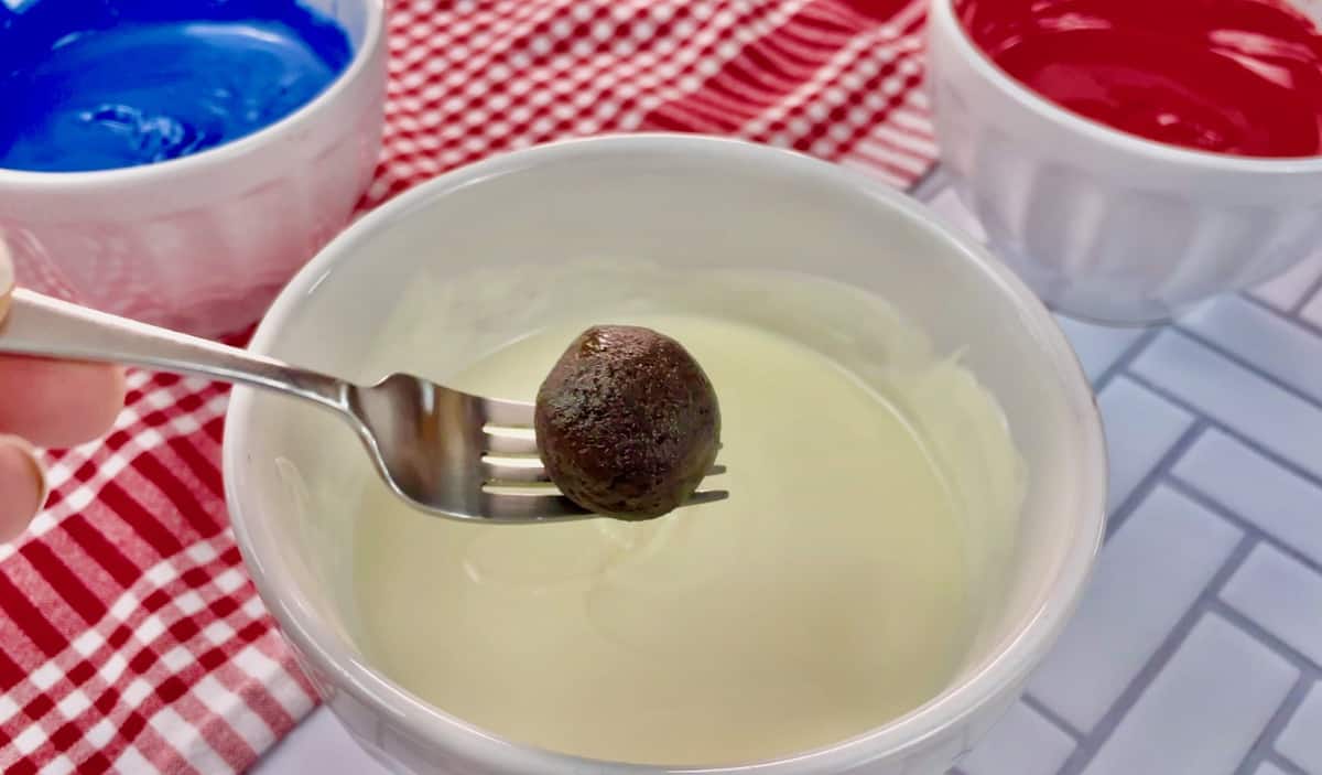 A fork holding an Oreo cream cheese ball and hovering over a bowl of melted almond bark.