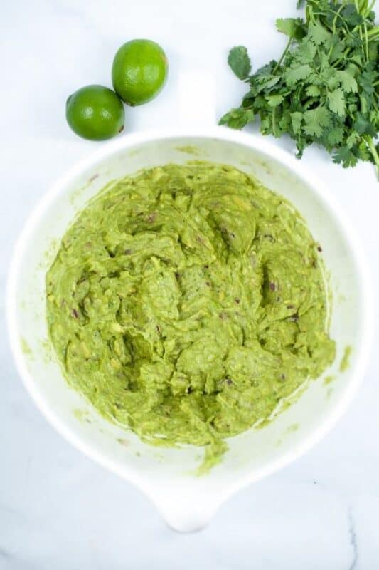 guacamole in a bowl with cilantro and lime on the table 