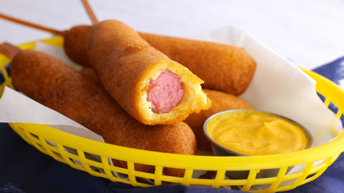 Bite taken out of a corn dog in a basket of corn dogs.