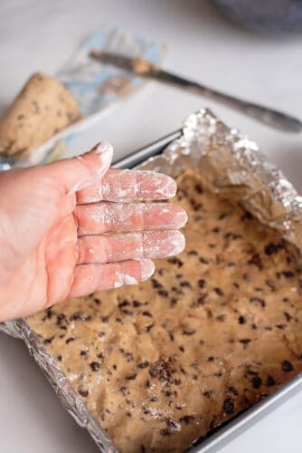 Floured fingers with pressed cookie dough on bottom of pan.