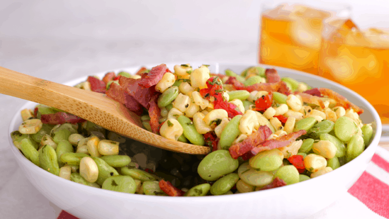 Wooden spoon scooping out serving of succotash.