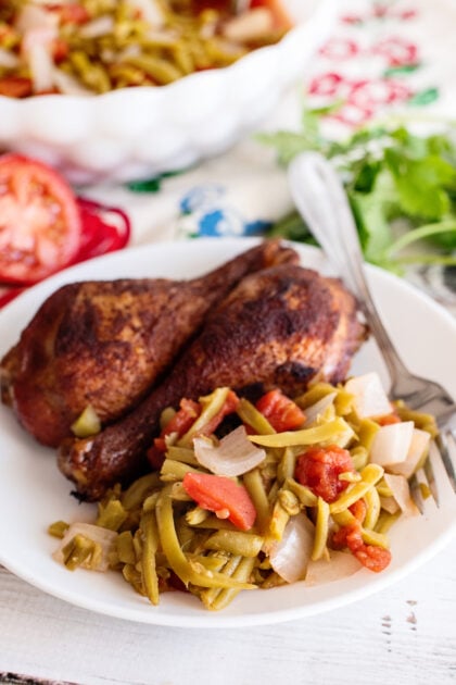 Green beans and tomatoes on plate with chicken legs.